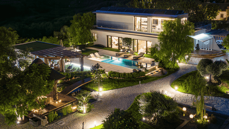 Luxury villa for sale in La Quinta illuminated at night, featuring modern architecture, a private swimming pool, landscaped gardens, and outdoor lounge areas