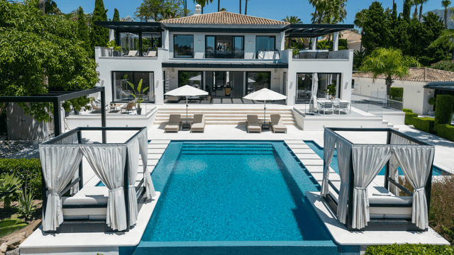 Luxury villa with a large swimming pool and stylish poolside cabanas, surrounded by lush greenery in Nueva Andalucia